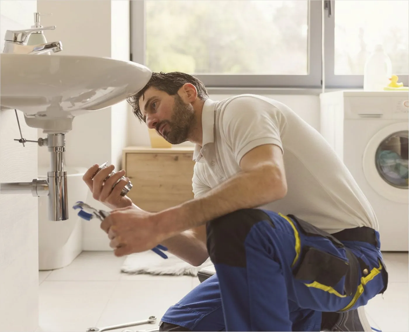 A plumber working on the pipes under a bathroom sink